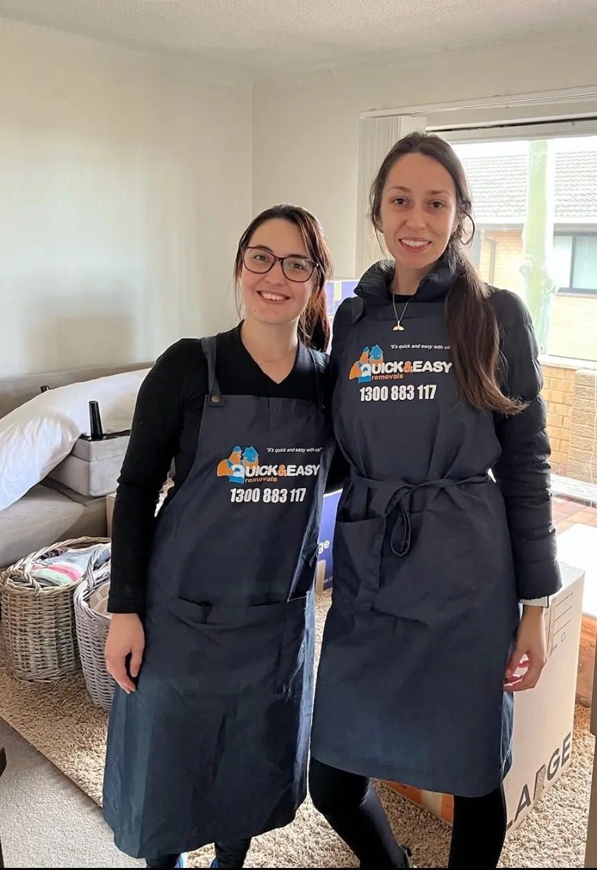 Two members of the Quick and Easy packing team in branded aprons beside a large moving carton