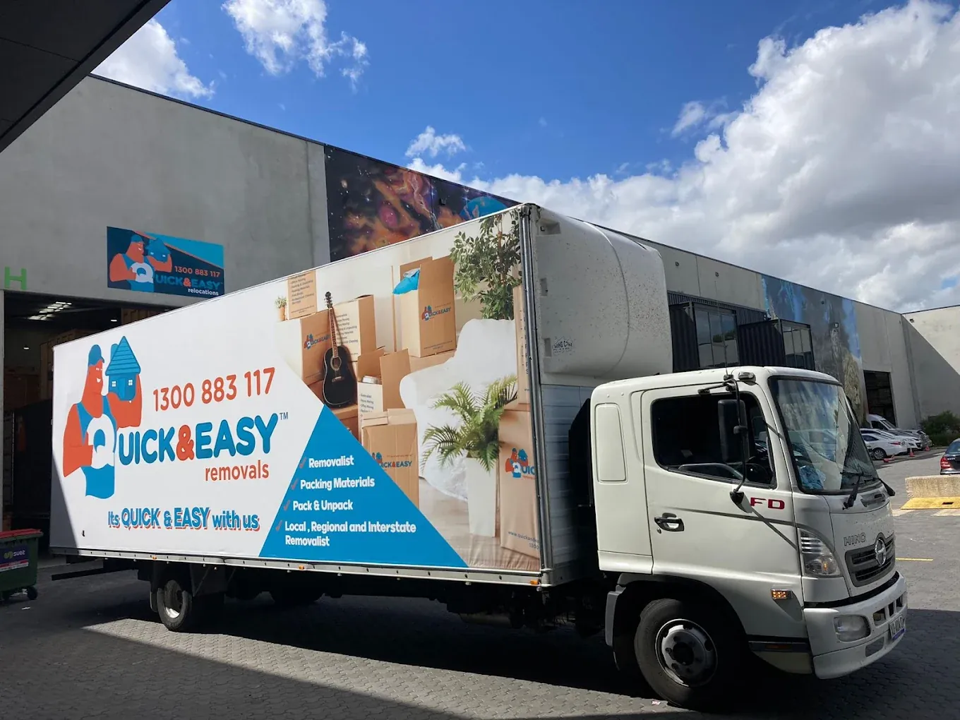 White Hino truck in the Quick and Easy Removals wrap parked side on outside the open depot roller door