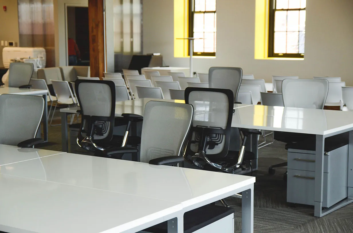 Empty open plan office with rows of white bench desks, mesh task chairs and pedestal drawers ready for a relocation