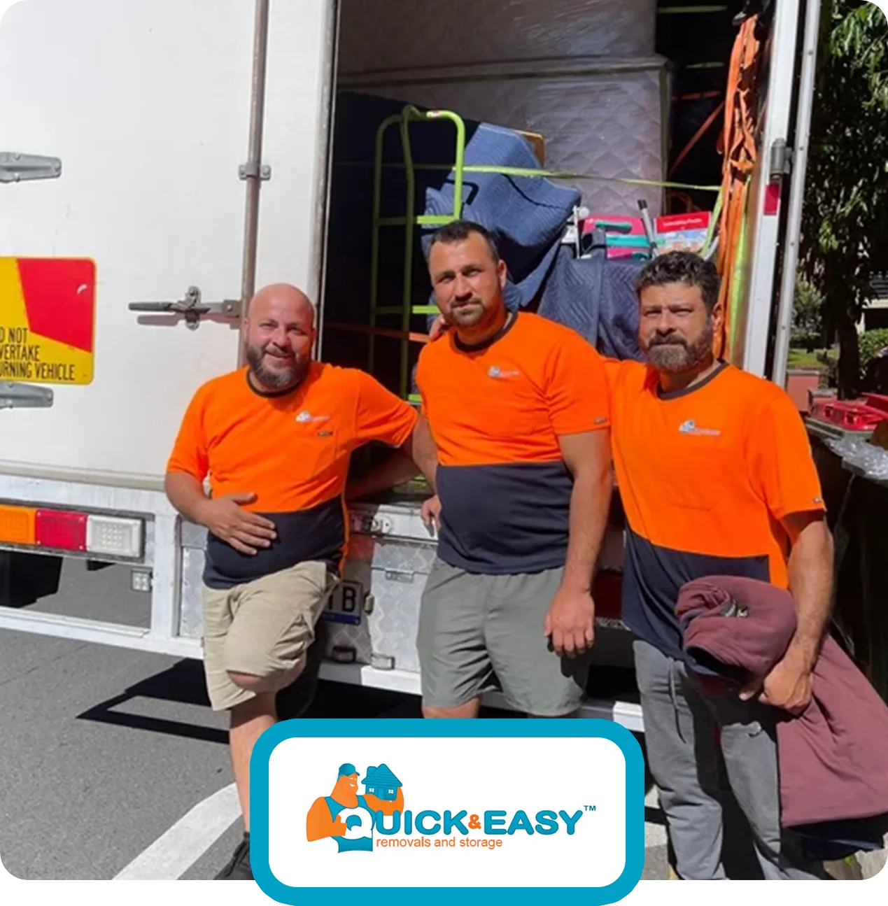 Three Quick and Easy crew members with trolleys and moving blankets at the open rear of a loaded truck