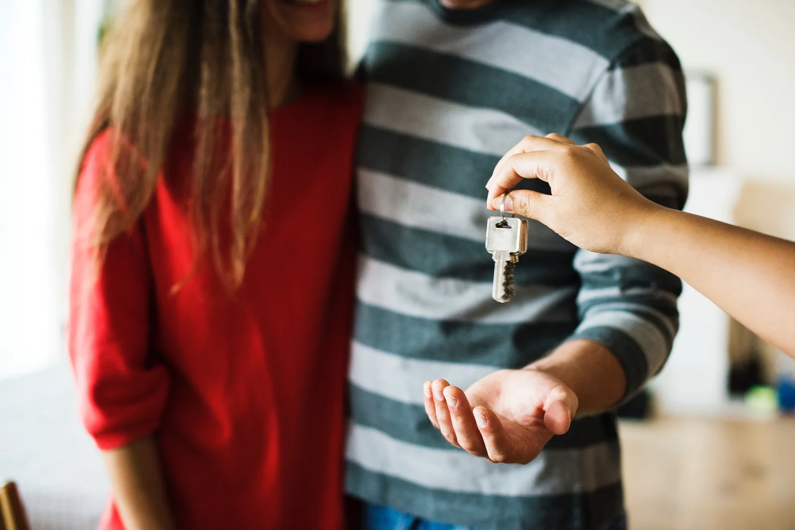 A set of house keys being handed to a man in a striped jumper standing beside a woman in a red top, with their faces out of frame
