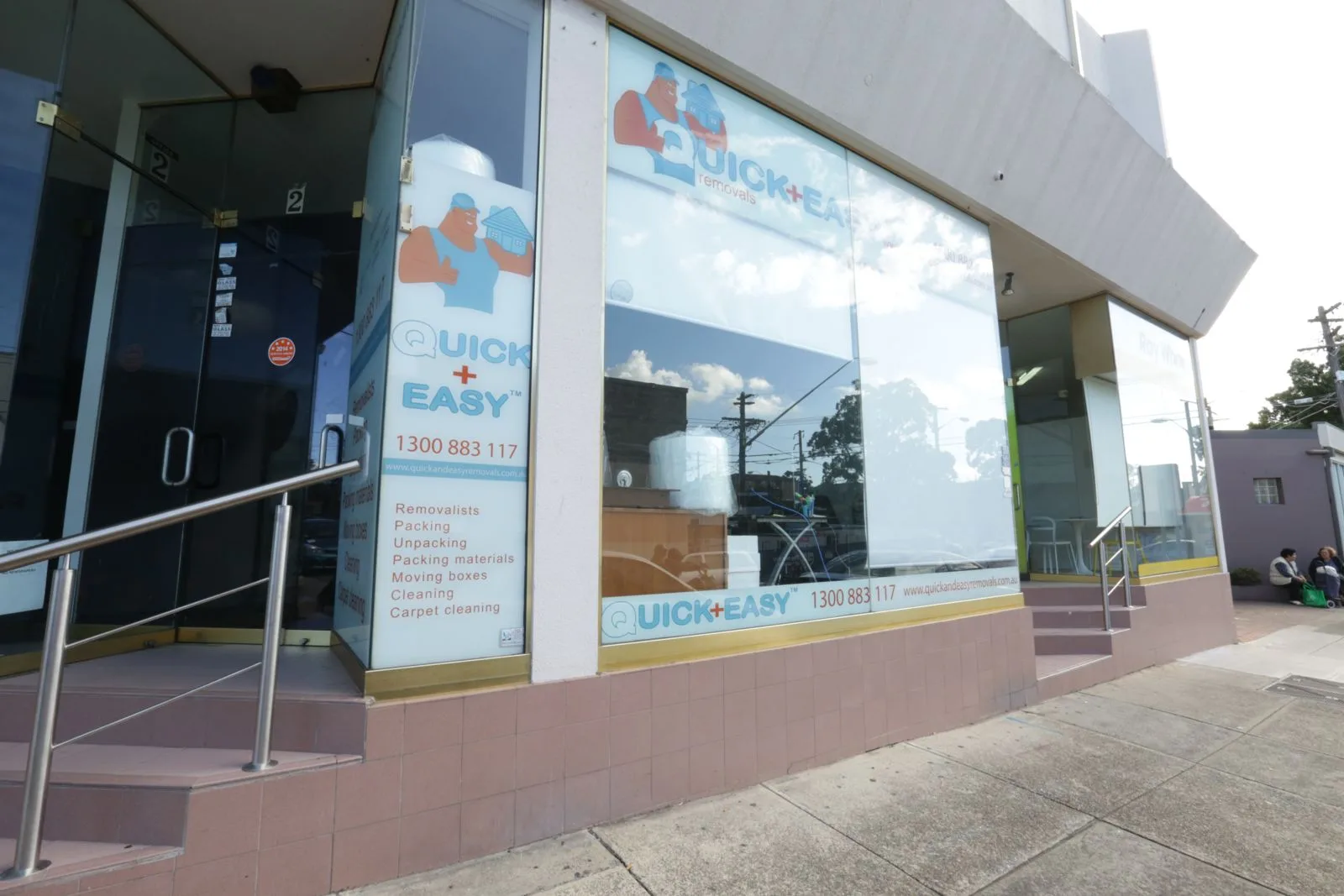 Street level view of the Quick and Easy Removals shopfront, with the 1300 883 117 phone number and a list of services on the glass