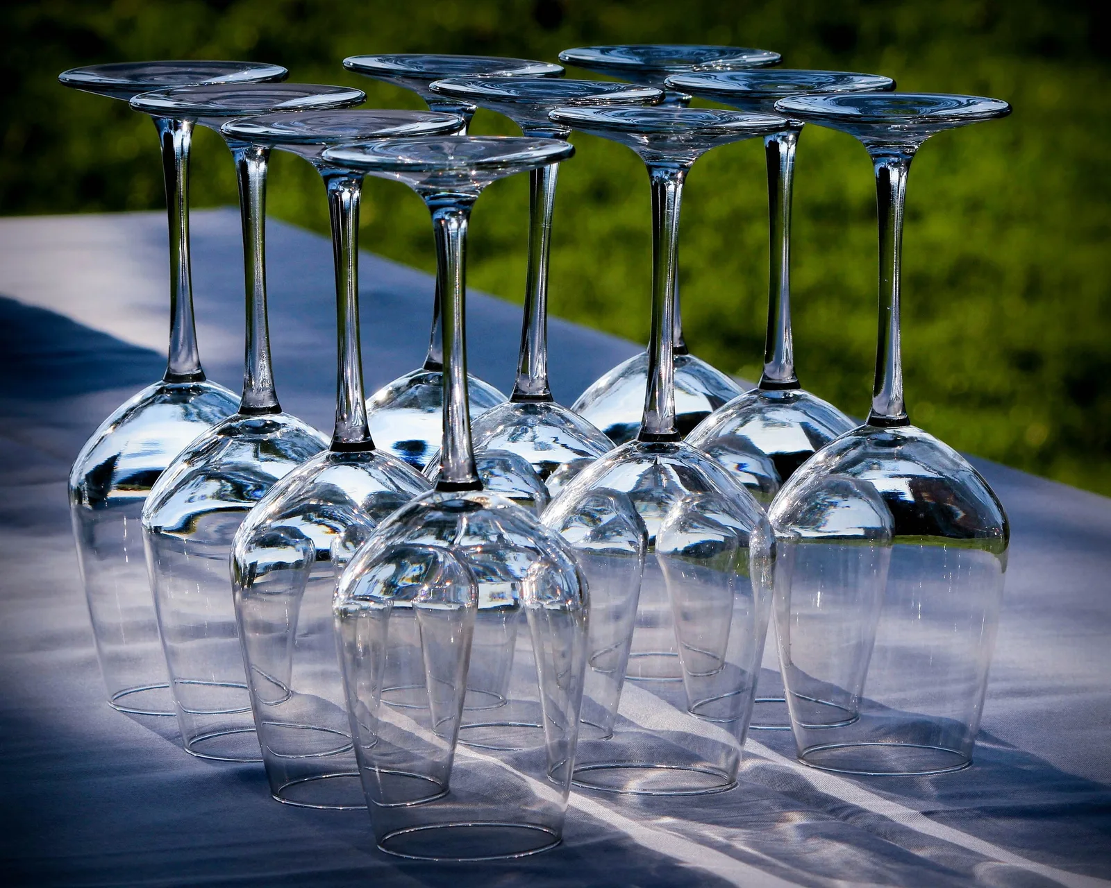 Rows of wine glasses standing upside down on an outdoor table in bright sunlight