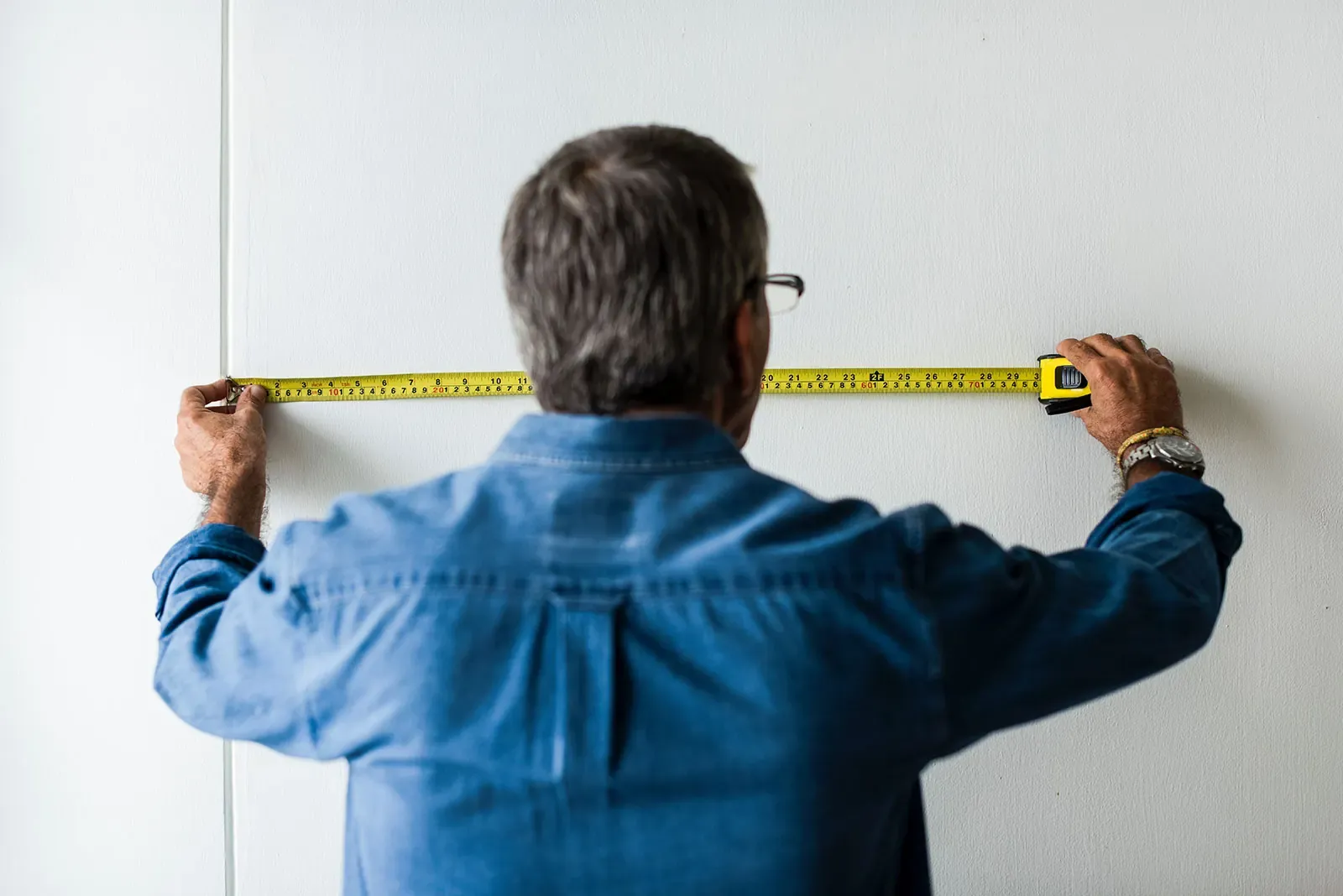 A person stretching a tape measure across a wall while measuring up before a move