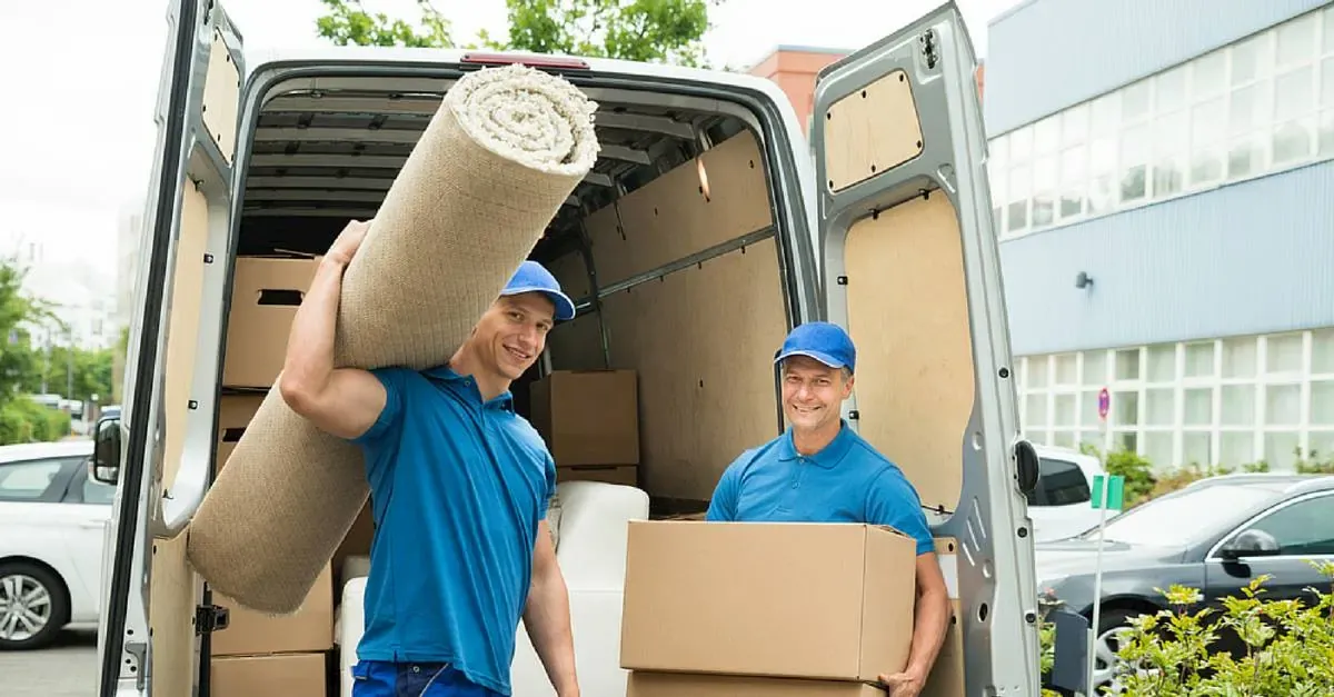 Two removalists at the open rear doors of a van loading a rolled rug and a carton
