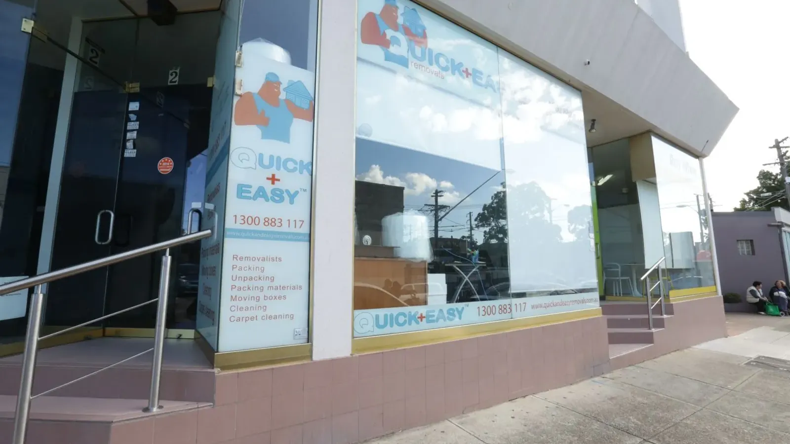 Street level view of the Quick and Easy Removals shopfront with the phone number and services listed on the glass
